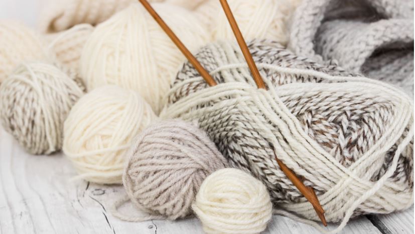 pile of cream- and brown-coloured balls of yarn with brown knitting needles
