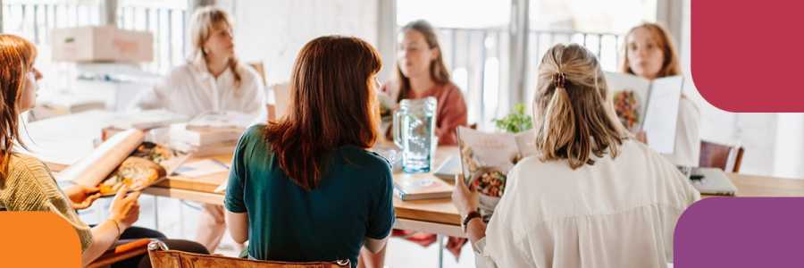 Adults sitting around a table holding cookbooks and talking.