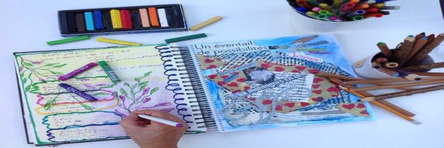 Personne dessinant dans un cahier posé sur une table et entouré de crayons