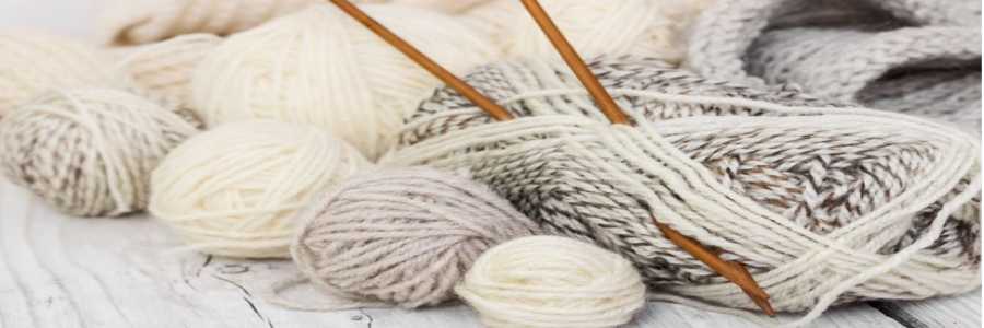 pile of cream- and brown-coloured balls of yarn with brown knitting needles
