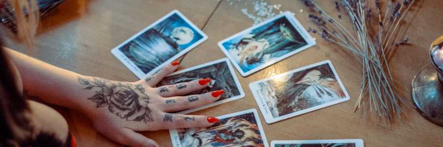 A mystical setup featuring tarot card reading on a wooden table, with artistic tattoos and dried flowers. Photo by Alina Vilchenko.